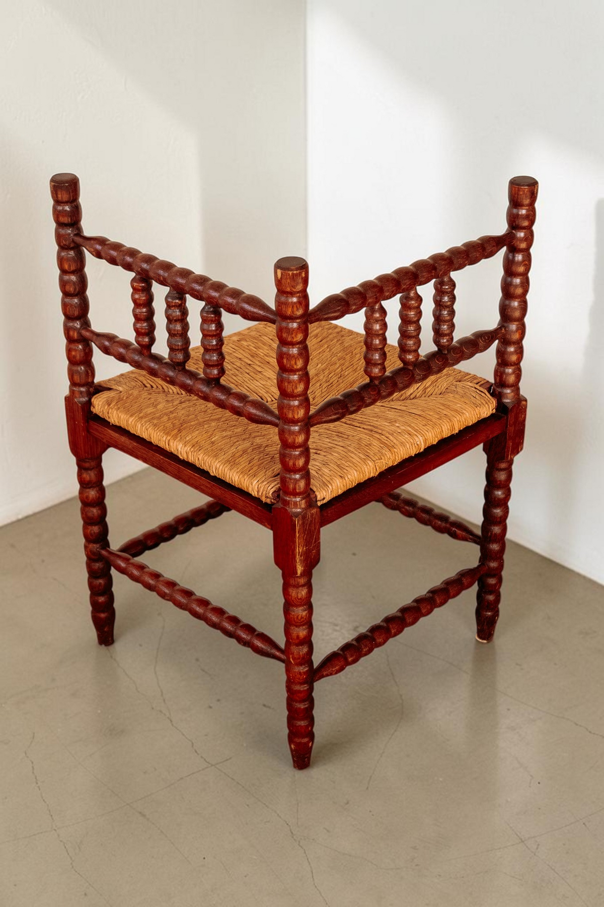 Antieke tessvintage hoekstoel van massief hout met bobbin details en een gevlochten rieten zitting.