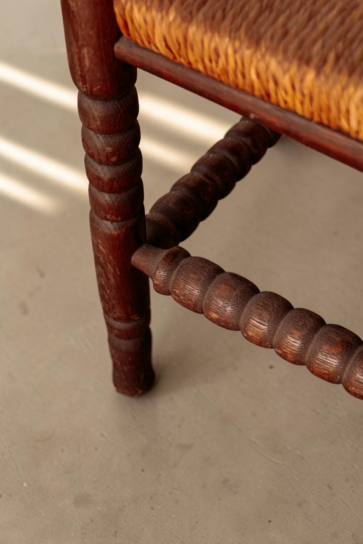 Detail van tessvintage houten bobbin hoekstoel met gedraaide poten en gevlochten rieten zitting