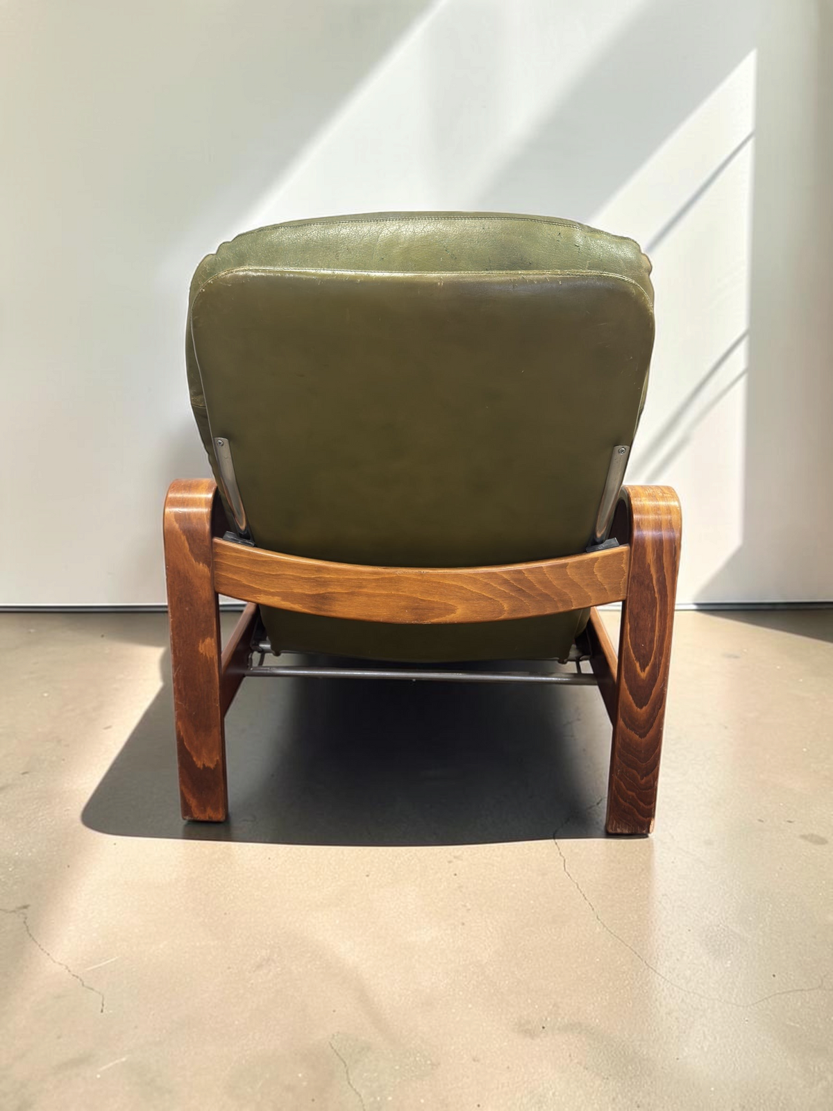 Achterkant van een vintage olijfgroene leren fauteuil van tessvintage met een frame van gebogen gelamineerd hout.