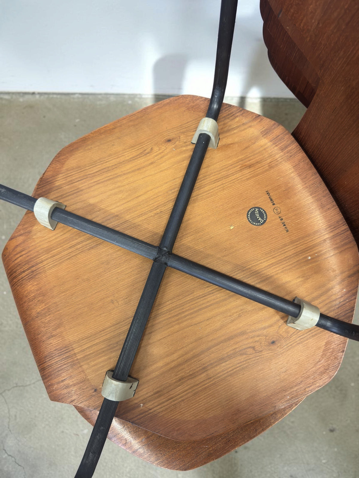 Onderkant van een vintage tessvintage Arne Jacobsen model 3103 T-stoel met teakfineer zitting en zwart metalen frame.