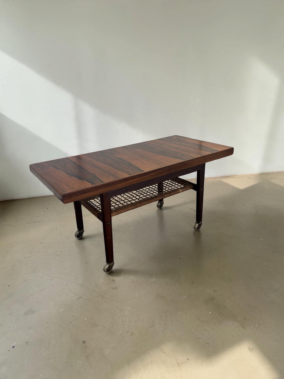 tessvintage Scandinavische salontafel van pallisanderhout met rotan lectuurrek en messing wieltjes uit de jaren 60
