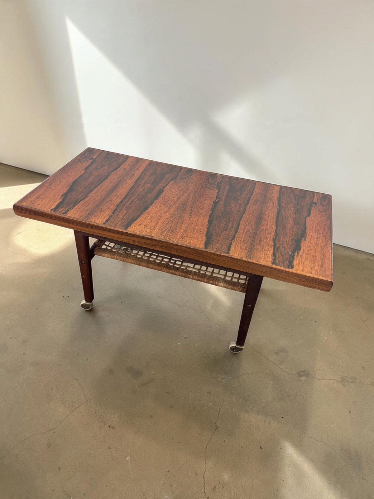 tessvintage Scandinavische salontafel van pallisanderhout met rotan lectuurrek en messing wieltjes uit de jaren 60
