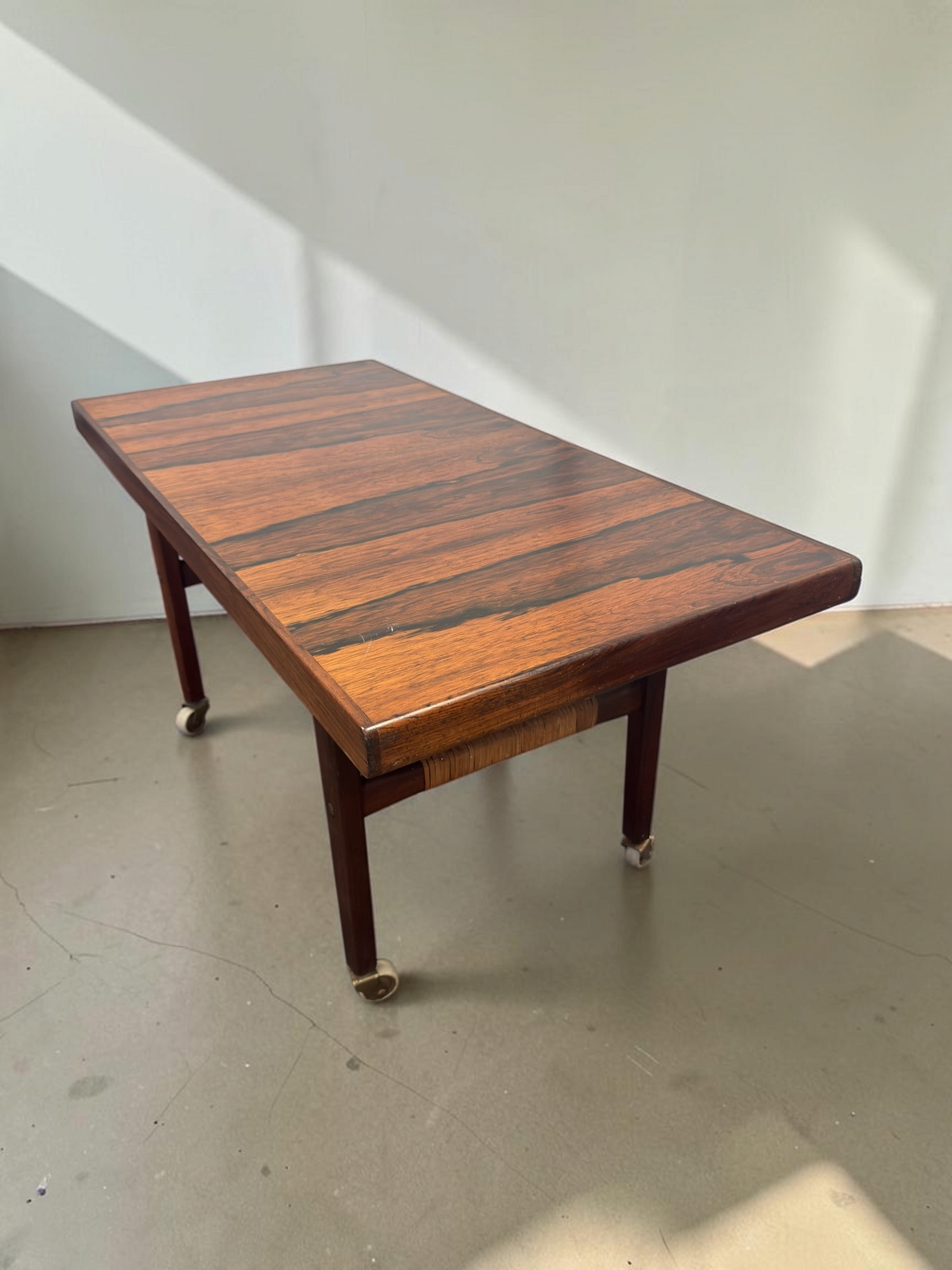 tessvintage Scandinavische salontafel van pallisanderhout met rotan lectuurrek en messing wieltjes uit de jaren 60