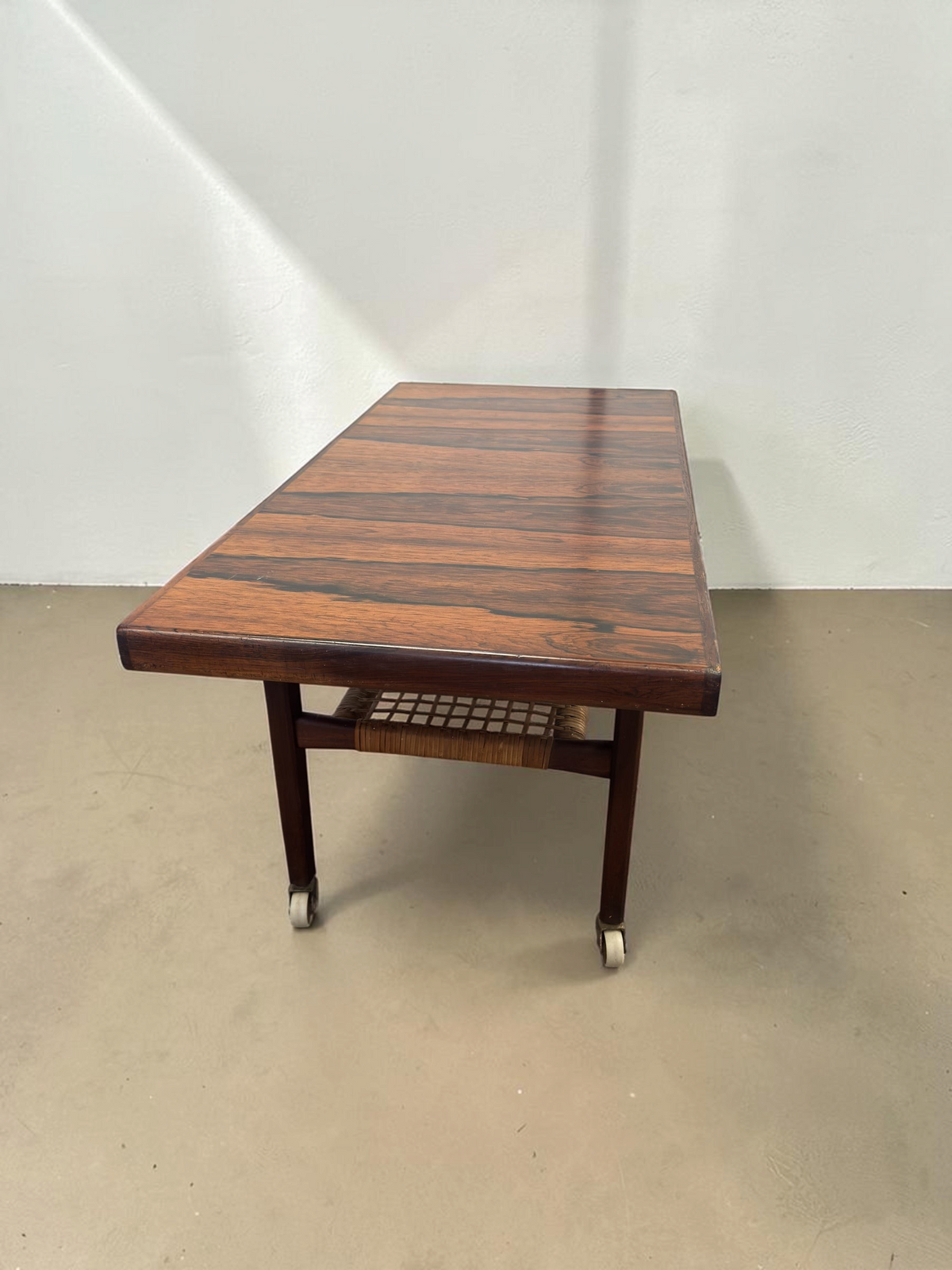 tessvintage Scandinavische salontafel van pallisanderhout met rotan lectuurrek en messing wieltjes