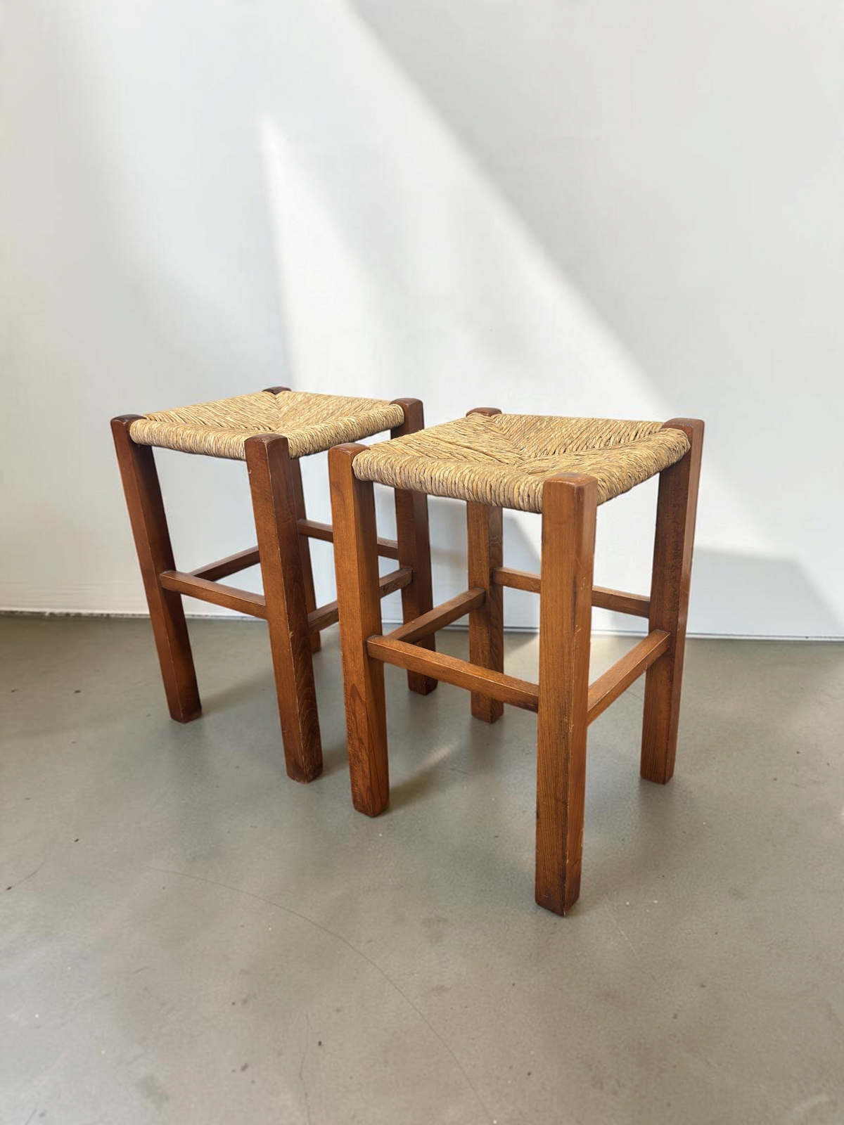 Set van twee tessvintage houten krukjes met een bruin frame en een gevlochten biezen zitting in visgraatpatroon.