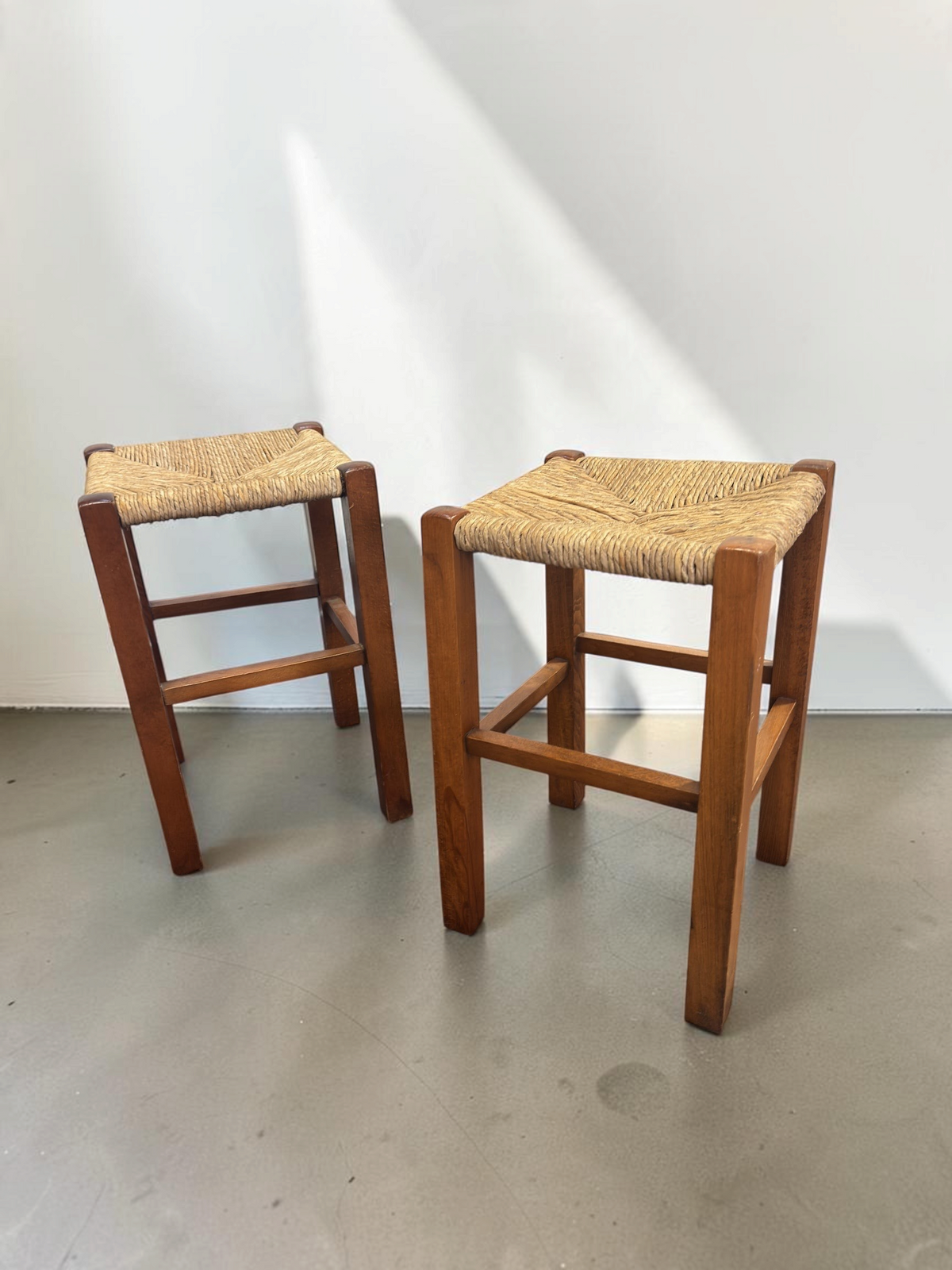 Set van twee tessvintage houten krukjes met een bruin frame en een gevlochten biezen zitting in visgraatpatroon.