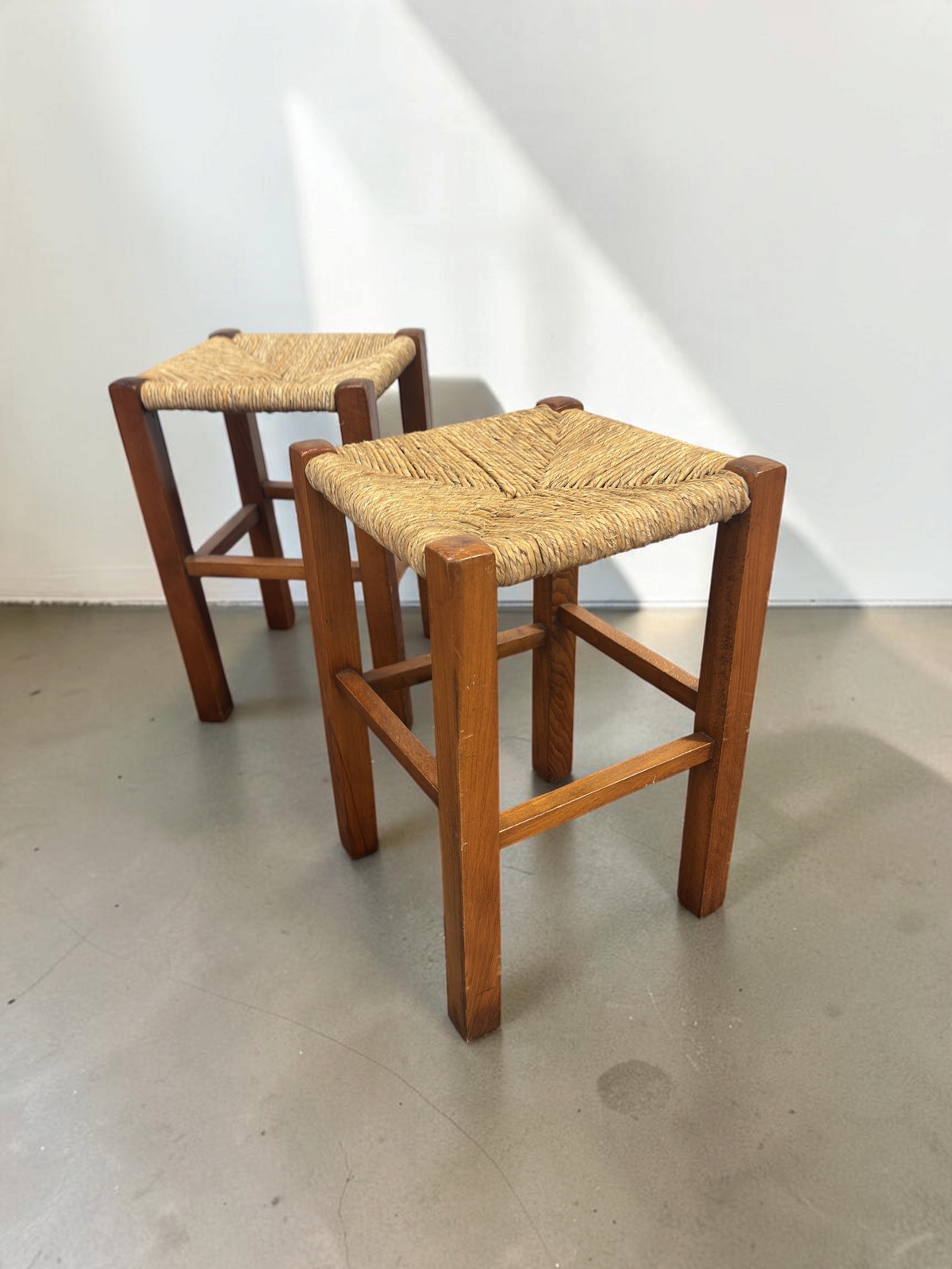 Set van twee tessvintage houten krukjes met een bruin frame en een gevlochten biezen zitting in visgraatpatroon.