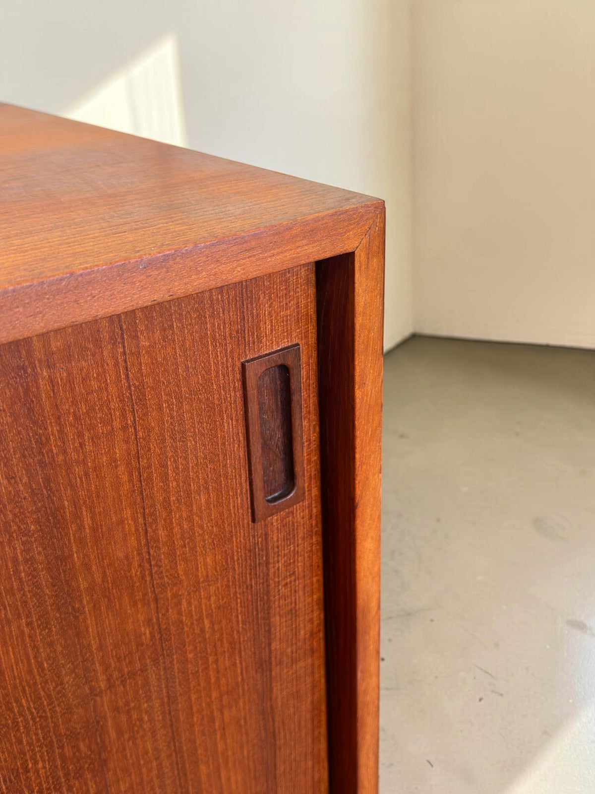 Detail van een tessvintage Deens teak dressoir met een verzonken houten handgreep op de schuifdeur.