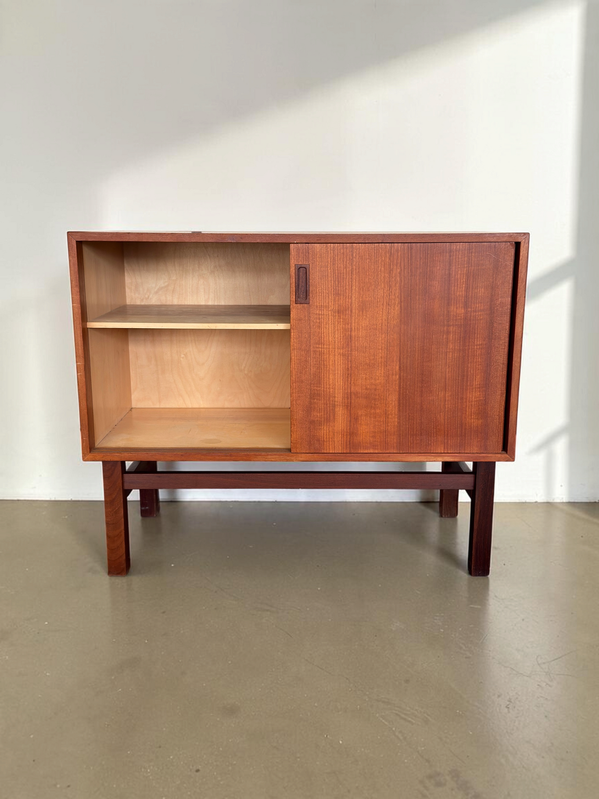 tessvintage Deens teak dressoir met schuifdeur, open vak met plank en donkerhouten H-frame onderstel