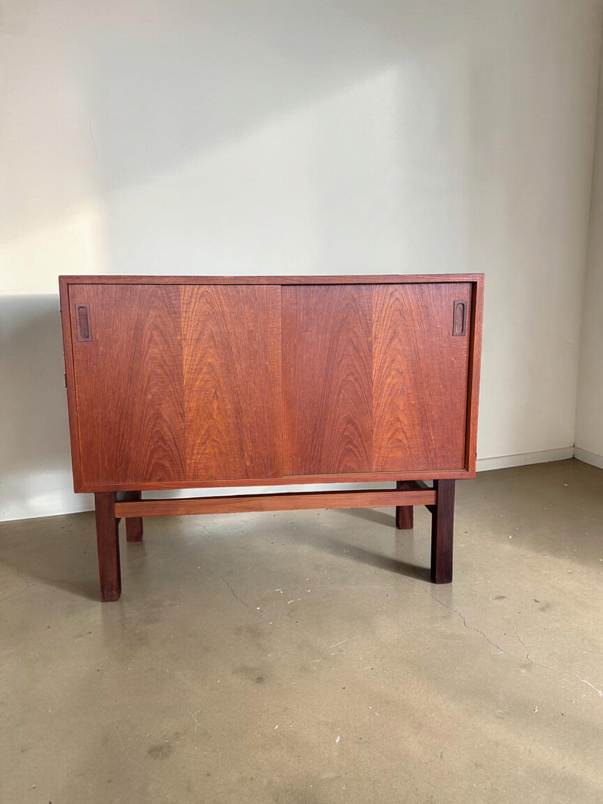 tessvintage Deens teak dressoir met schuifdeuren en een donkerhouten H-frame onderstel in een strak vintage design.