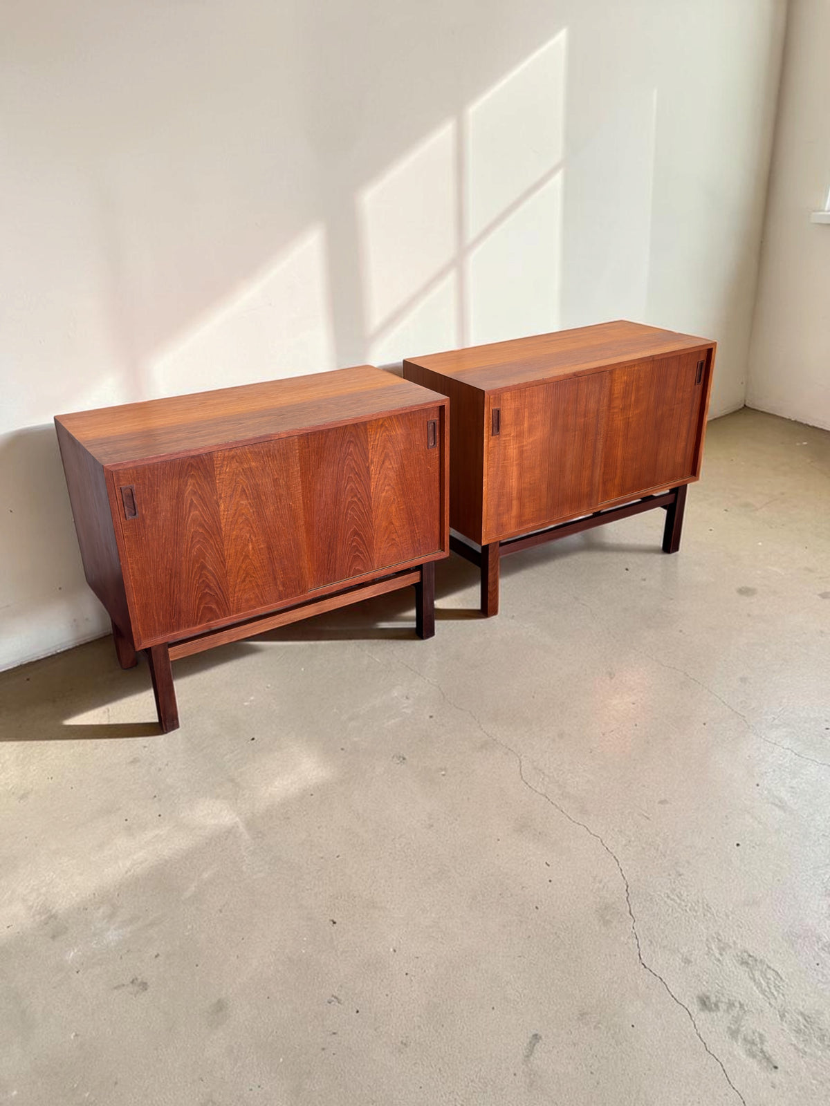 Twee tessvintage Deense teak dressoirs met schuifdeuren en een strak H-frame onderstel in een lichte ruimte.