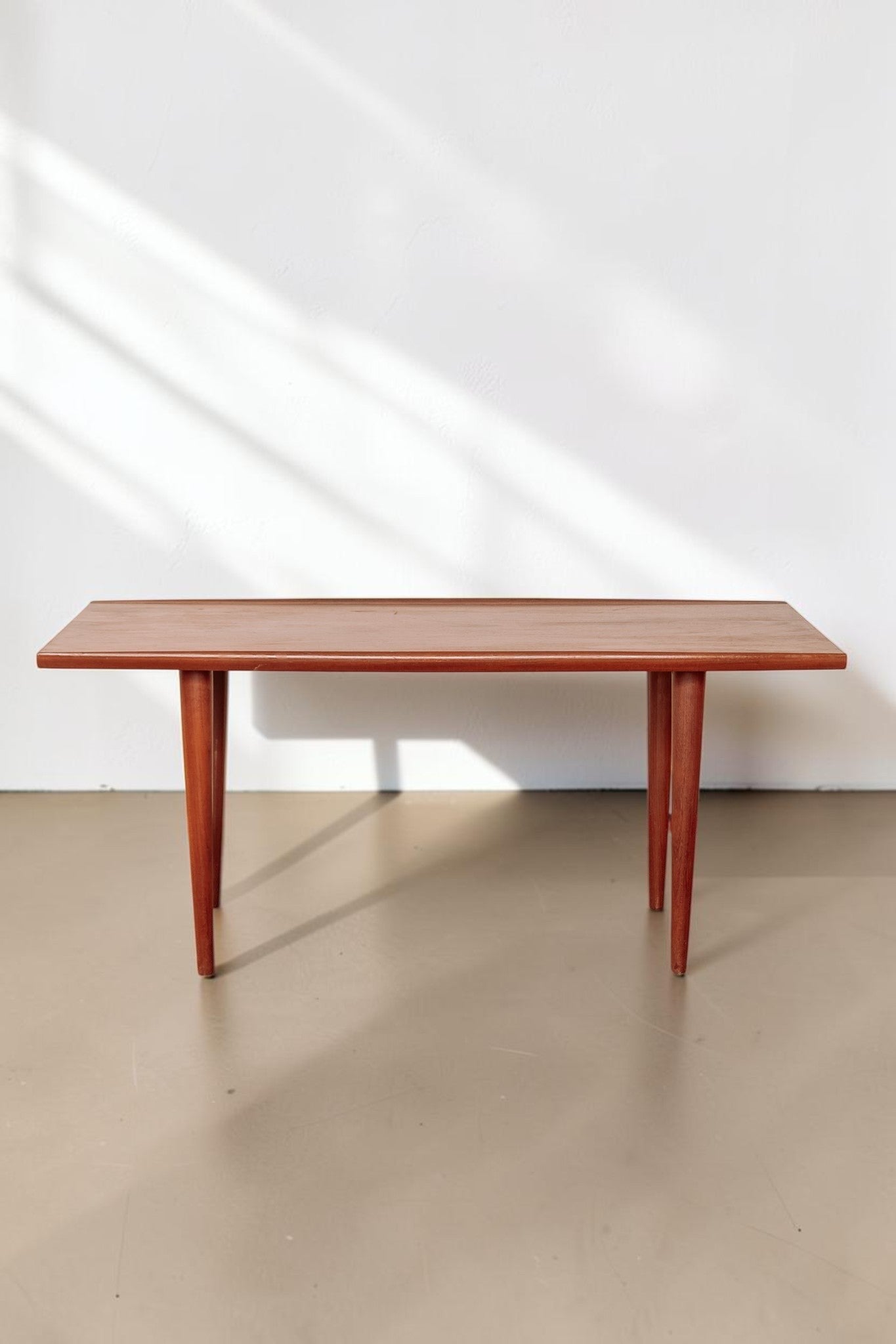 tessvintage mid-century modern teak coffee table with rounded edges and tapered legs in a warm wood finish
