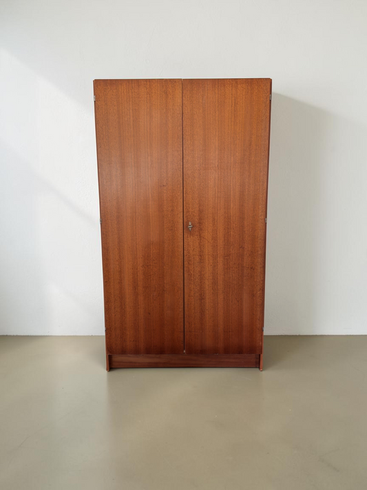 tessvintage vintage garderobekast van teakfineer met twee deuren en slot, staand tegen een witte muur